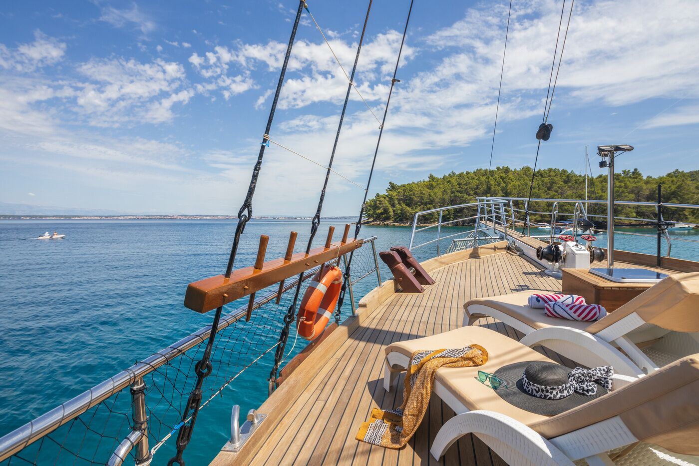 A deck with lounge chairs, a lifebuoy, and a view of the sea and distant land.