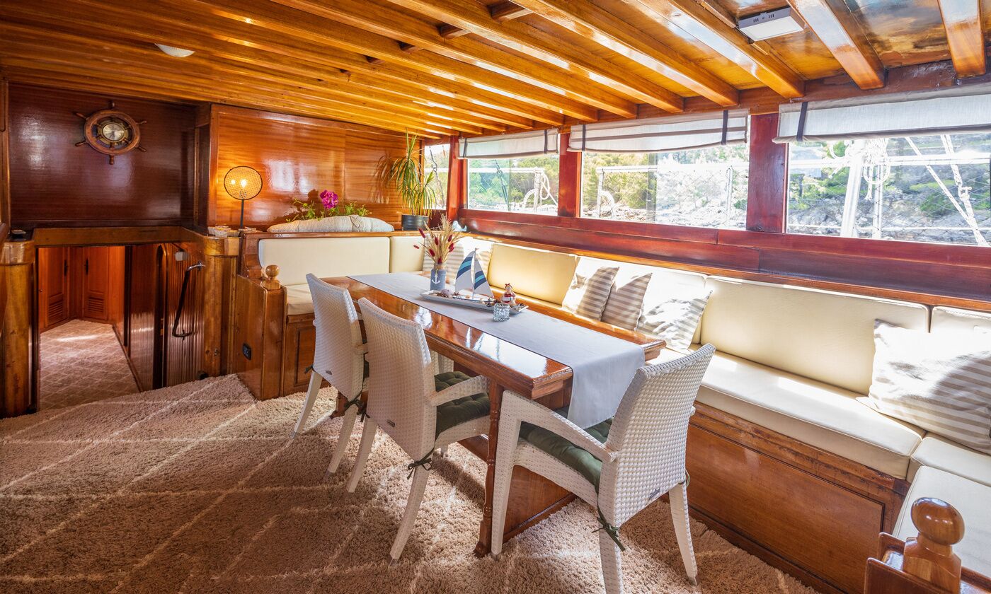 A wooden interior with a dining table, chairs, a bench, and a window with a view.