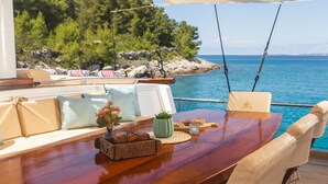 A boat deck with a wooden table, cushions, a vase with flowers, a suitcase, and a bag. - Sun-Kissed Sailing Adventure in Split, Croatia (Kaštel Gomilica)