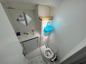 Et lille badeværelse med håndvask, spejl, toilet og en blå vask.