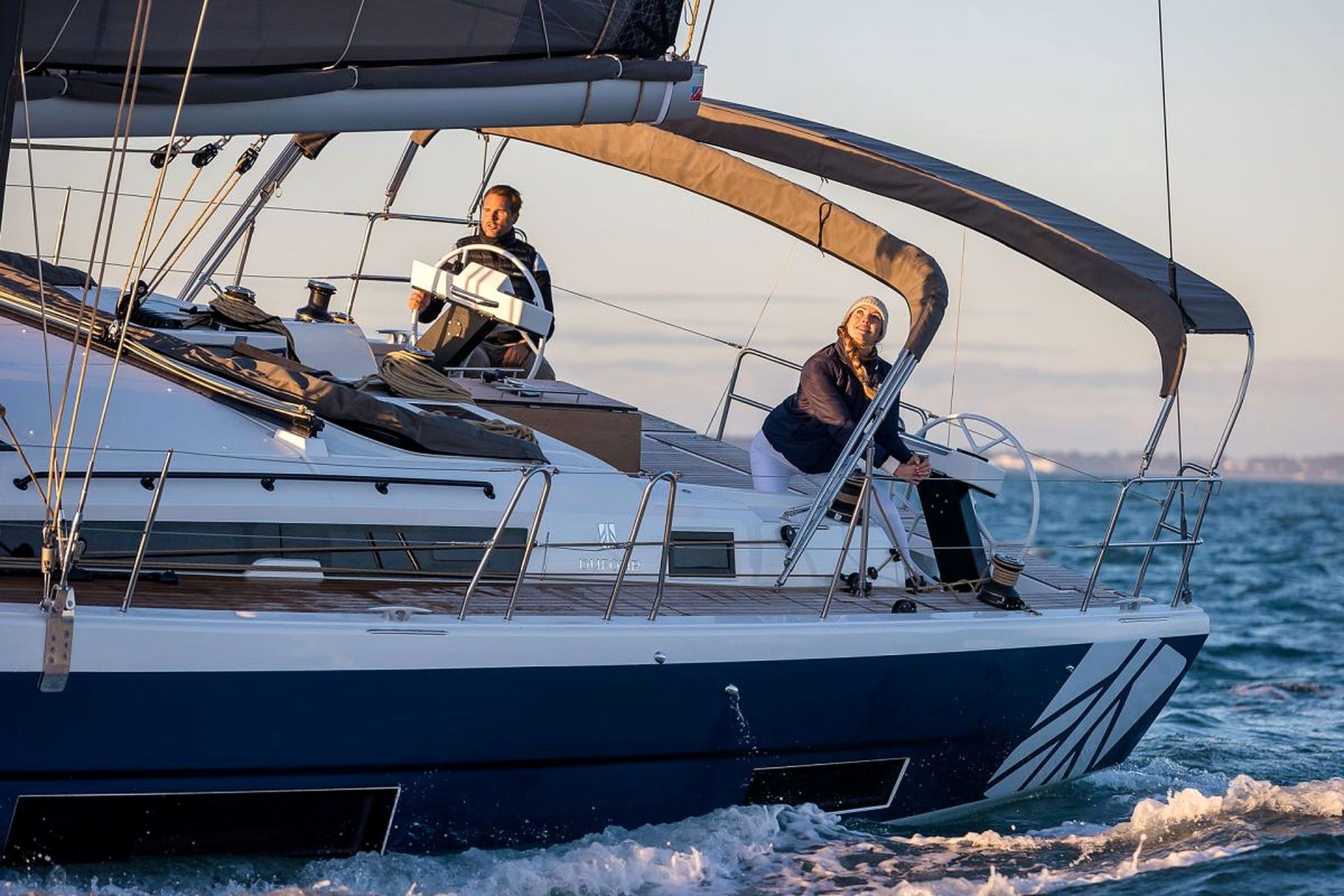 A sailboat with two people on deck, one steering and one on the bow.