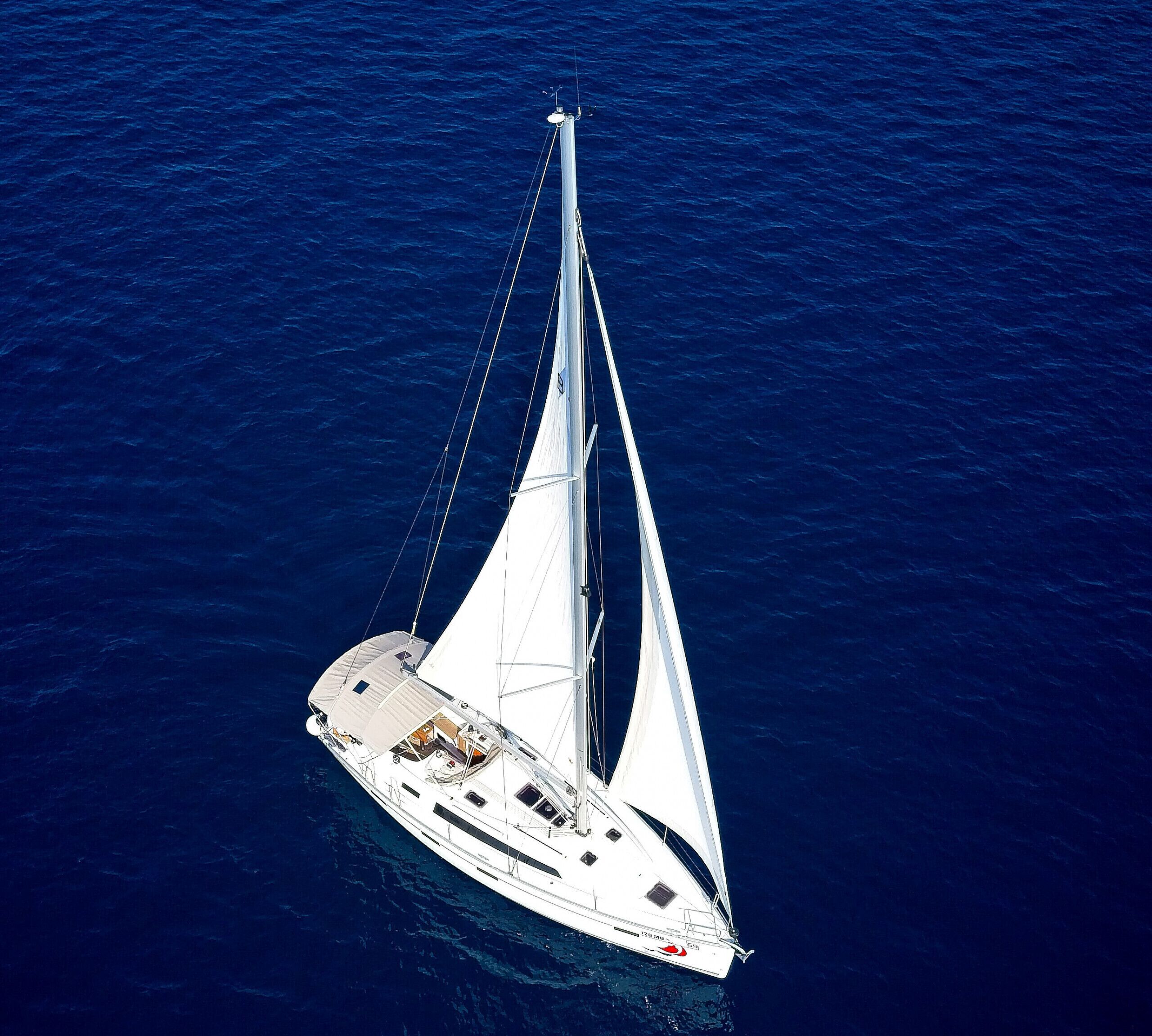 Una barca a vela bianca con cabina e posti a sedere sul ponte, che naviga in un mare blu intenso.