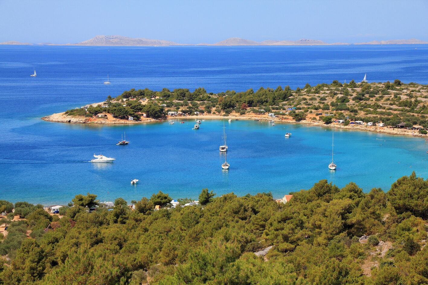 A coastal area with boats, a small settlement, and dense green vegetation.