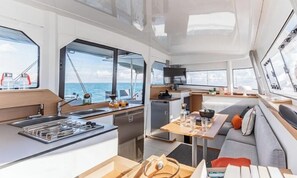 Une cuisine moderne dotée d’un îlot central, d’un coin repas avec un canapé et de grandes fenêtres offrant une vue sur la mer.