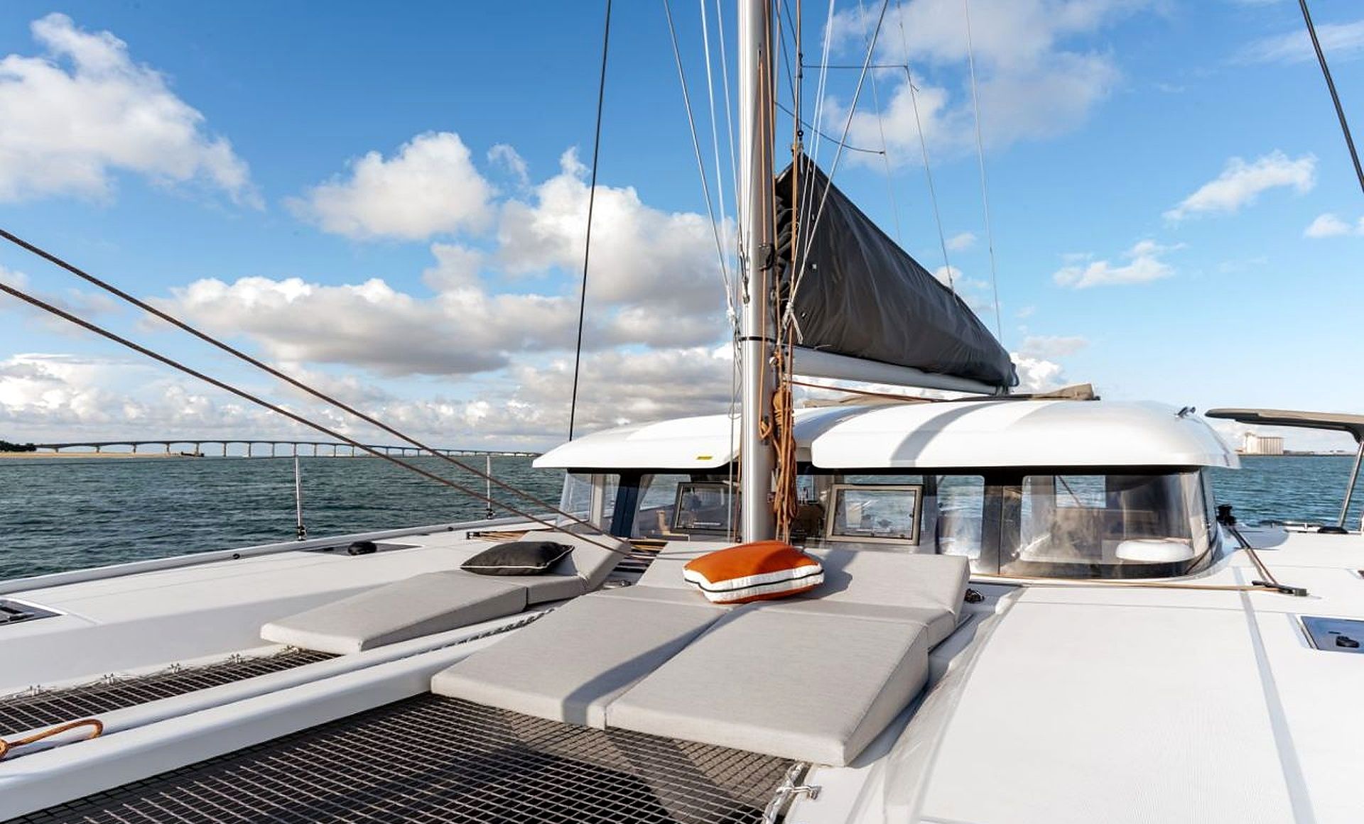 A sailboat with a covered deck area, a mast, and a view of the water and a bridge in the background.