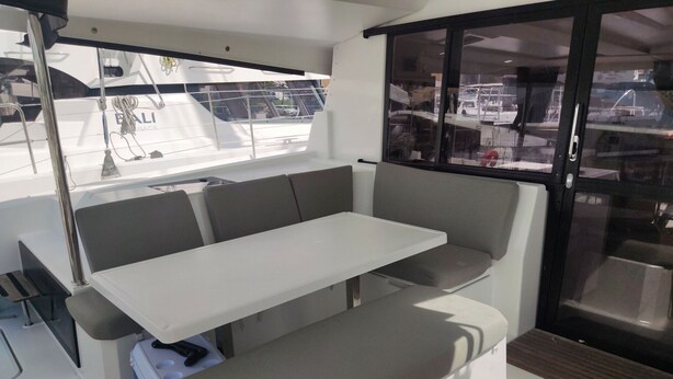 Un interior moderno con una mesa blanca y asientos grises, ventanas amplias y una puerta corredera.