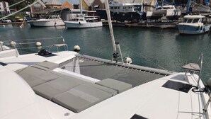 Un puerto deportivo con barcos amarrados, un barco blanco con cojines grises y una vista despejada del agua.