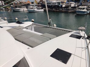 Een jachthaven met aangemeerde boten, waaronder een witte boot met grijze kussens, en een helder uitzicht op het water.
