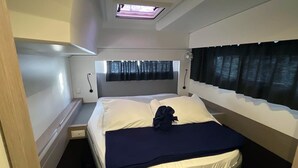 Un dormitorio compacto con cama, tragaluz, ventana con cortinas y mesita de noche.