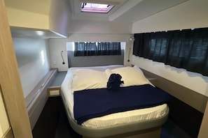 Een compacte slaapkamer met een bed, dakraam, raam met gordijnen en een nachtkastje.