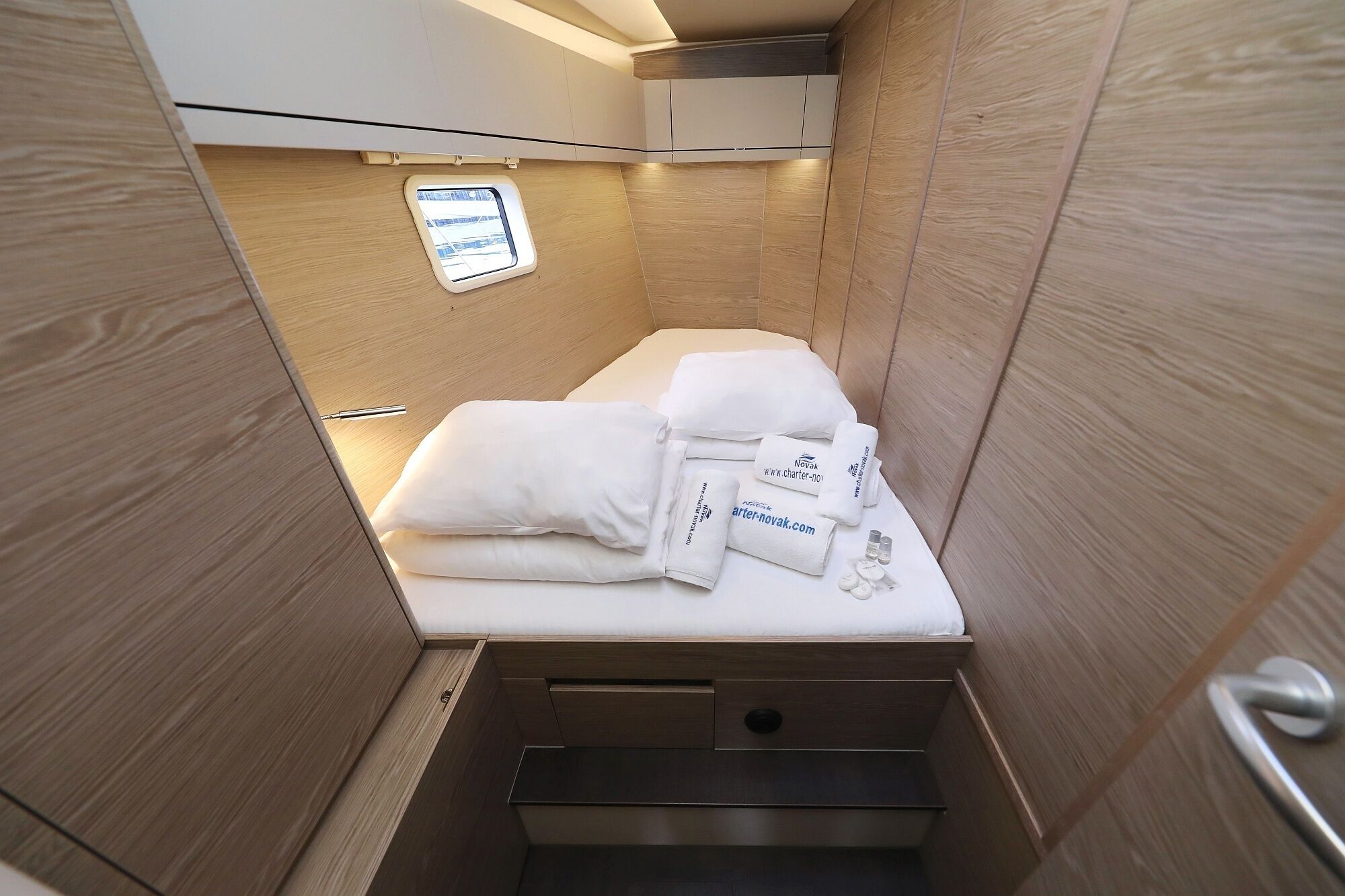 A compact, modern room with a bed, neatly folded towels, and a small window.