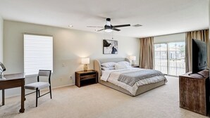 Ein Schlafzimmer mit Bett, Schreibtisch, Stuhl, Deckenventilator und Fernseher.
