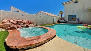 Ein Garten mit Schwimmbad, Whirlpool und einer Steinmauer.