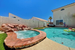 Ein Garten mit Schwimmbad, Whirlpool und einer Steinmauer.