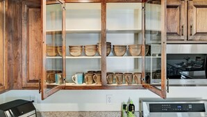 Eine Küche mit Holzausstattung, einem eingebauten Schrank mit Glastür und Keramikgeschirr, einer Mikrowelle und einer Kaffeemaschine.