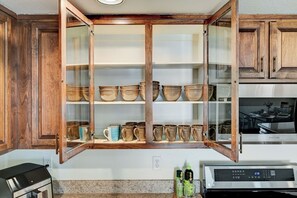 Eine Küche mit Holzausstattung, einem eingebauten Schrank mit Glastür und Keramikgeschirr, einer Mikrowelle und einer Kaffeemaschine.