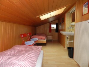 Ein schmaler, holzgetäfelter Raum mit zwei Betten, einem Waschbecken und einem Fenster.