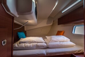 A compact bed with white bedding and a teal pillow, a small window with a view, and a wooden headboard. - Sun-Kissed Sailing: An Unforgettable Beach Experience in Istria, Croatia (Medulin)