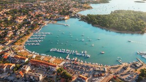 Vista aèria d'una població costanera amb un port esportiu, edificis i una illa boscosa.