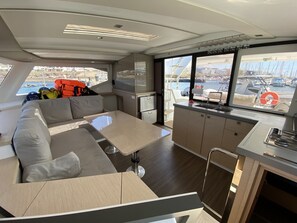A modern interior with a sofa, table, and kitchen area, featuring a view of boats and water.