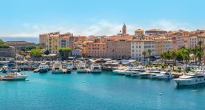 A marina with boats docked, a historic town with colorful buildings, and a prominent tower in the background.