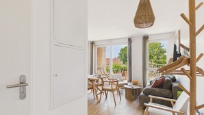 Un salon moderne avec un coin repas, de grandes fenêtres et un porte-manteau en bois.