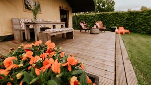 A wooden deck with outdoor seating, a covered area, and a garden with orange flowers. - Kampari - Luxury Safari Tent - Out of Africa (Delfstrahuizen)