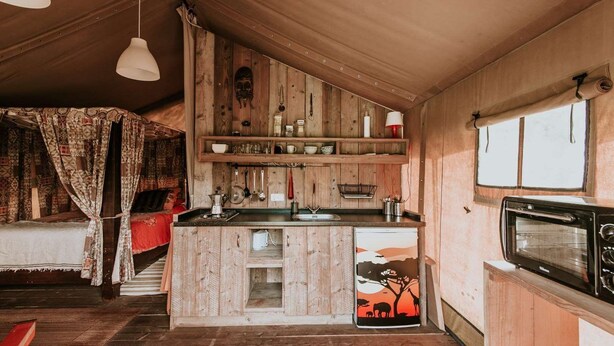 A compact kitchen with wooden cabinets, a built-in microwave, and a small refrigerator. - Kampari - Luxury Safari Tent - Out of Africa (Delfstrahuizen)