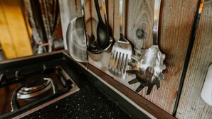 A kitchen with a wooden backsplash, a gas stove, and various utensils hanging on the wall. - Kampari - Luxury Safari Tent - Out of Africa (Delfstrahuizen)