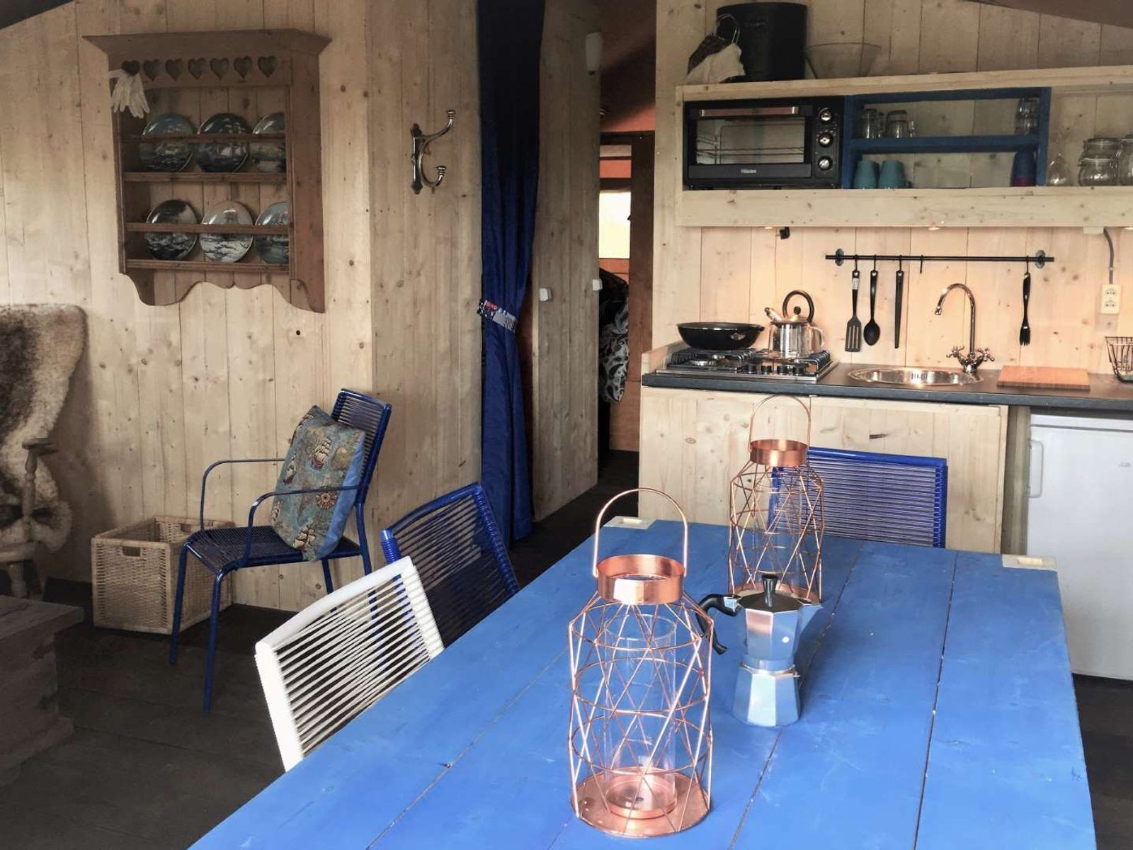 Une cuisine rustique aux murs en bois, avec une table bleue et des lanternes en cuivre.