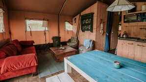 En ombonad inredning med en soffa, ett bord, en stol, en lampa och ett litet kök.