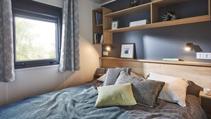 A bedroom with a bed, bedside tables, a shelf with books and a picture, and a window with curtains. - Kampari - Tiny House - Bosk (Delfstrahuizen)
