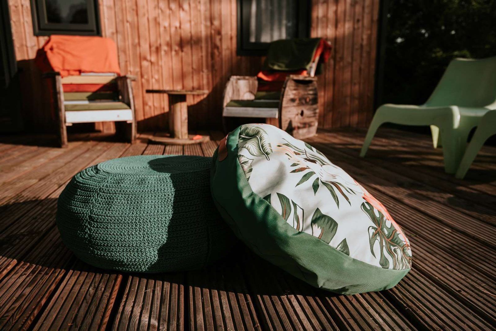 Two green ottomans with floral patterns on a wooden deck.