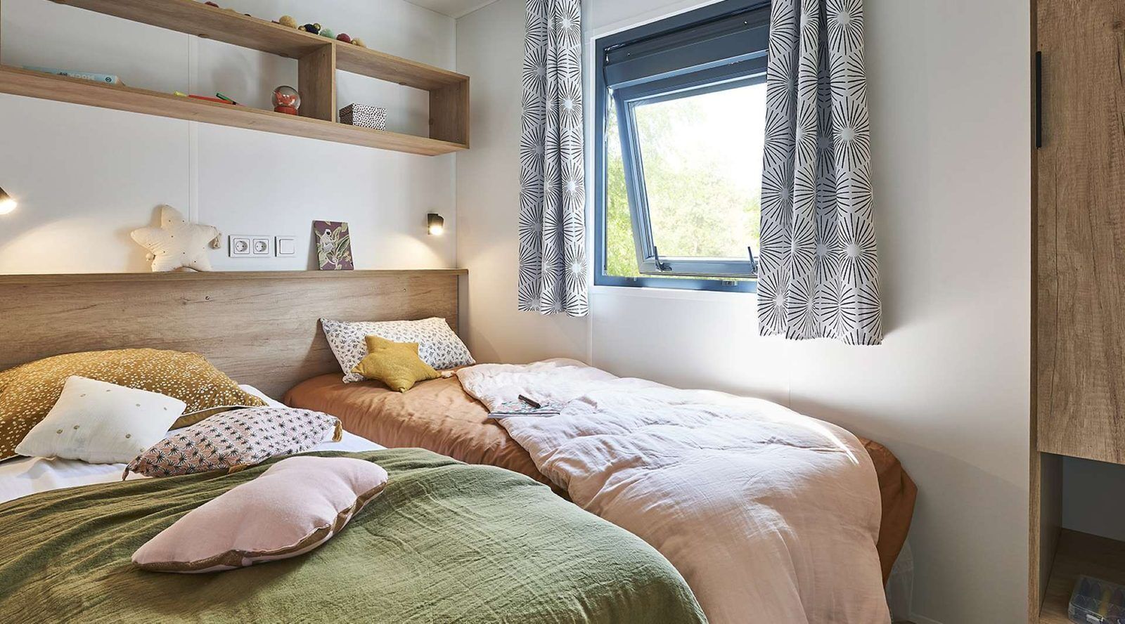Een slaapkamer met twee bedden, een houten hoofdbord, een plank met decoratieve objecten, een raam met gordijnen met patroon, en een zeesterdecoratie aan de muur.
