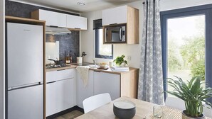 A modern kitchen with white cabinets, a built-in microwave, and a window with patterned curtains. - Kampari - Tiny House - Bosk (Delfstrahuizen)