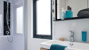 A bathroom with a shower, a sink with a towel, and a window. - Kampari - Tiny House - Bosk (Delfstrahuizen)