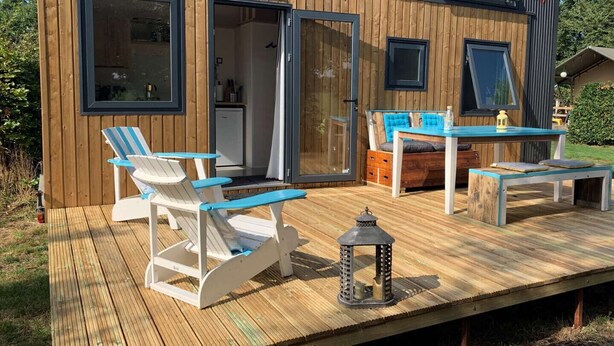 Eine Holzhütte mit einer Terrasse, einem Essbereich mit Stühlen und einem Tisch sowie einer kleinen Küche.