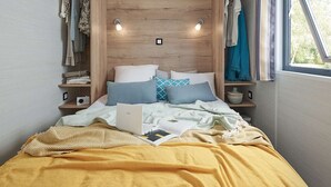 Ein Bett mit Laptop, Kissen und Decke. Regale mit Kleidung und einem Radio.