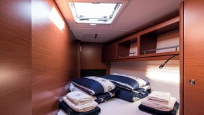 Un interior compacto y bien iluminado con tragaluz, una cama con toallas ordenadas y muebles de madera.