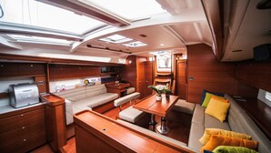 Interior de un yate con comedor, asientos, cocina y zona de preparación de alimentos.