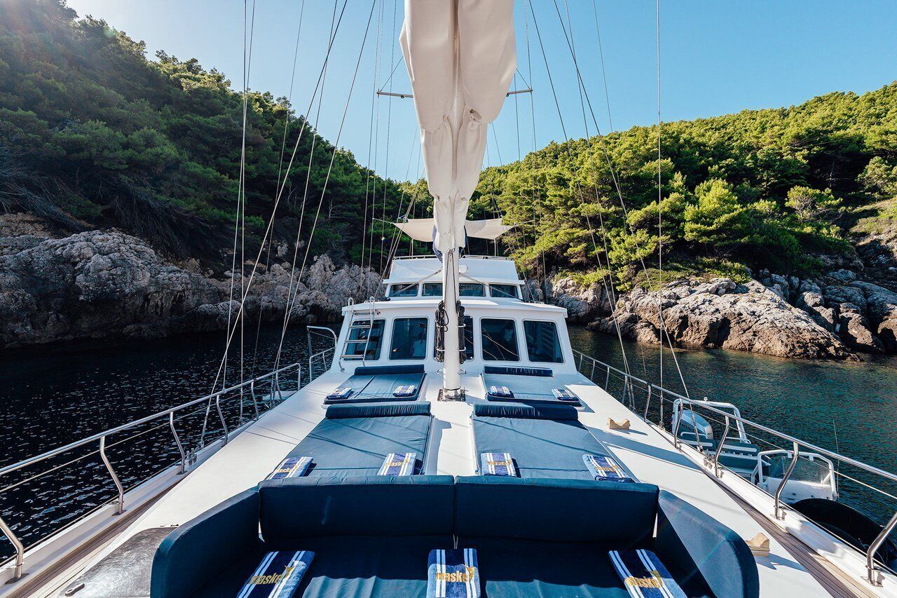 A boat with a cabin, lounge area, and a view of rocky coastline and greenery.