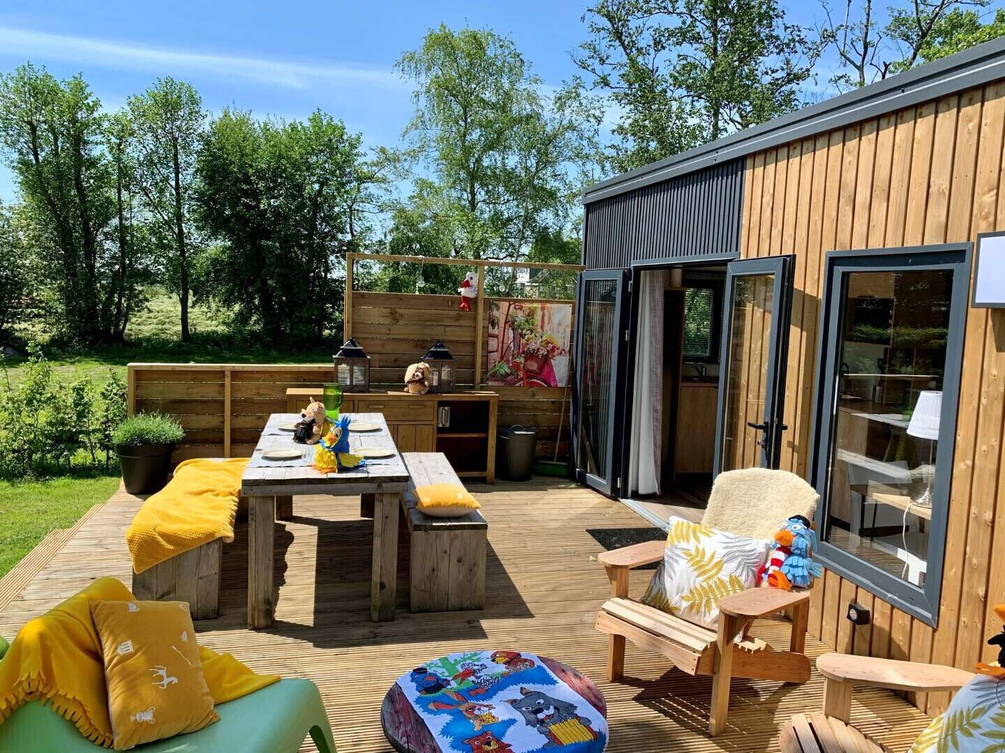 Une terrasse en bois avec une table et des chaises, un petit canapé et une pièce avec des fenêtres.