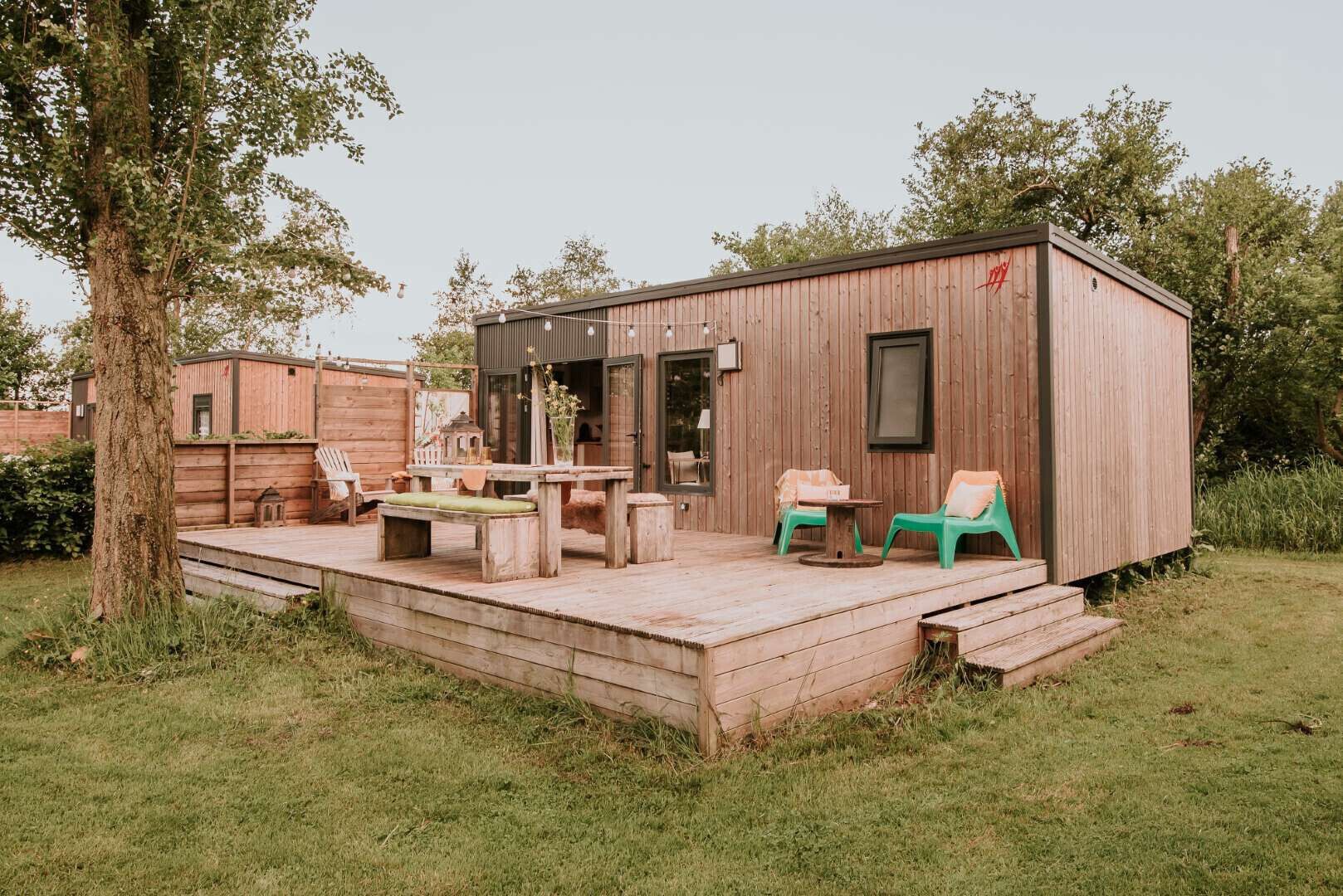 A wooden cabin with a deck, a table, chairs, and a small window.