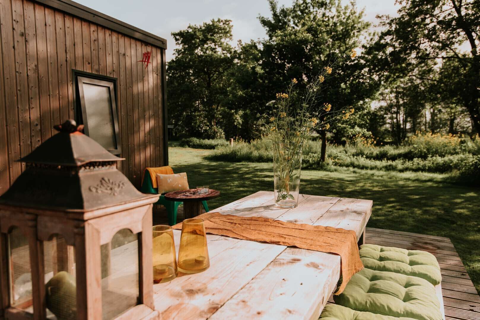 An outdoor seating area with a wooden table, chairs, a lantern, and a vase of flowers.