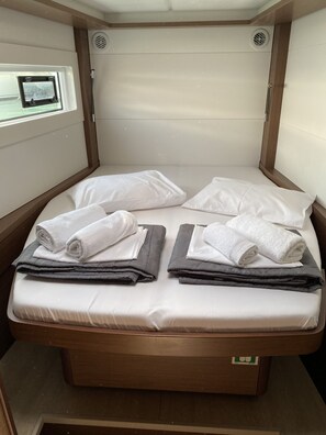 A bed with white linens and rolled towels, a window with a view, and a wooden headboard. - Sun-Kissed Sailing Adventure in Islas Sarónicas (Alimos)