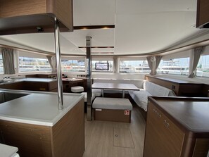 A compact galley with a sink, stove, and seating area, featuring a view of the marina through large windows. - Sun-Kissed Sailing Adventure in Islas Sarónicas (Alimos)
