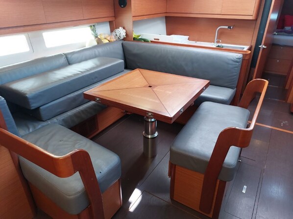 A compact kitchenette with a wooden table, two chairs, a sofa, and a small sink. - Sun-Kissed Sailing Adventure in Phuket (Mai Khao)