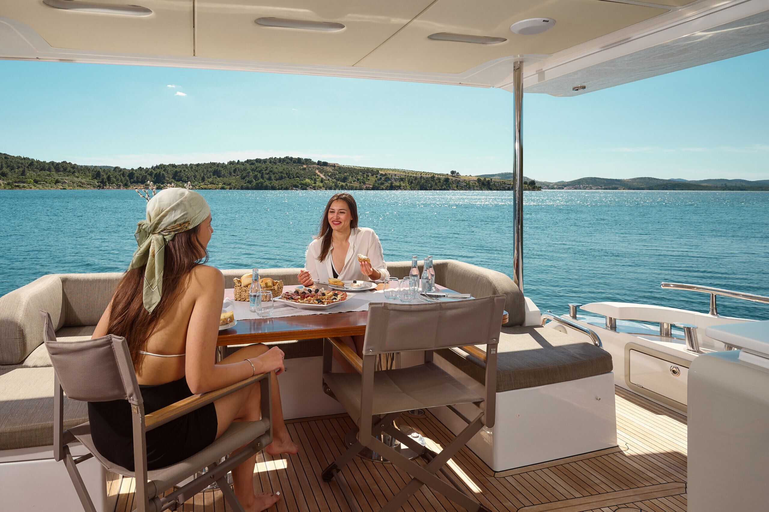 A boat deck with a table set for two, a view of a lake, and a distant shoreline.