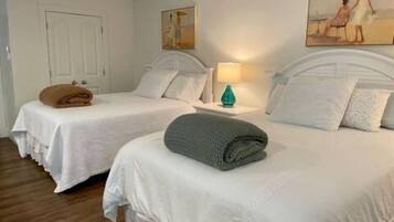 Habitación de hotel con dos camas, una puerta, un cuadro en la pared y una mesita de noche con una lámpara.