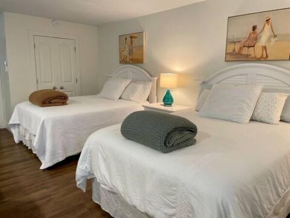 Een hotelkamer met twee bedden, een deur, een schilderij aan de muur en een nachtkastje met een lamp.